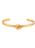 Gold cuff bracelet with twisted rope texture and decorative knot centerpiece on cream background.