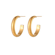 Chunky tubular hoop earrings in warm 14K gold-plated finish with smooth polished surface on cream background.